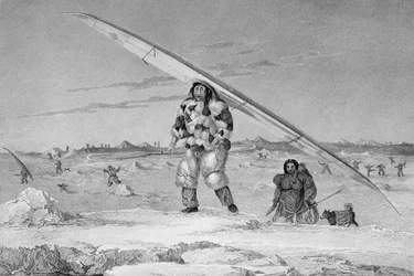 Un esquimal de Igloolik, con una chaqueta de piel de ave, llevando su canoa al agua, de 